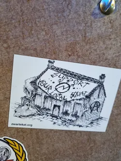 Street sticker Black and white illustration of a squat building with a banner saying "Support your local squat".  The sticker features a hand-drawn style and includes the website zwartekat.org.