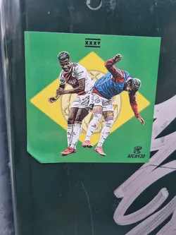 Street sticker A sticker depicting a football match scene between Antony and Lisandro Martínez. The illustration style is reminiscent of trading cards or limited-edition prints. The sticker has a green background with yellow accents, and a small logo 'AFCA420' is visible in the bottom right corner. The text 'XXXV' is featured at the top.