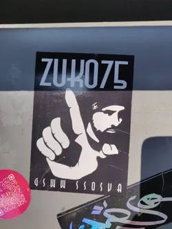 Black and white sticker featuring a stylized hand gesture and the text ZUKO75.  There is additional text at the bottom that is partially visible. 