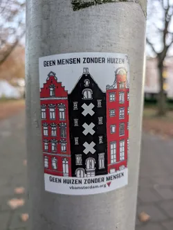 Street sticker The sticker features a stylized depiction of three Dutch canal houses. The two outer houses are bright red with white window frames and intricate architectural details, including stepped gables. The central house is black and features the three St. Andrew's crosses, a prominent symbol of Amsterdam, in white. The houses are rendered in a graphic, somewhat simplified style with black outlines. The sticker has a white background and is affixed to a metal pole.