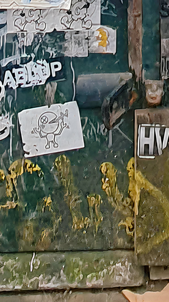 This sticker showcases a cartoon figure with a crossed-out eye, happily devouring an airplane. It's part of a collection of stickers and remnants layered on an old green wall.
