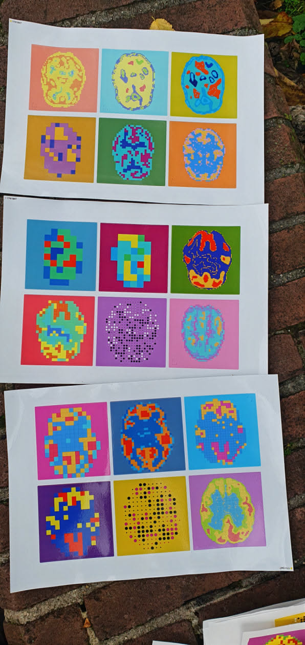 The image showcases three sheets of paper, each displaying a grid of colorful, pixelated brain illustrations. These prints combine a retro, digital aesthetic with anatomical imagery, possibly exploring themes of mind, technology, or art.