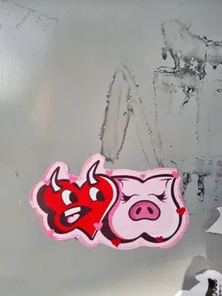 Street sticker A sticker featuring a cute cartoon devil heart and a pig face. The heart is red with small horns and a mischievous expression, while the pig is pink and has long eyelashes. Both characters are surrounded by small pink hearts.
