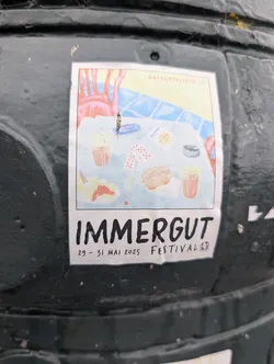 Street sticker A sticker promoting the IMMERGUT FESTIVAL, scheduled for May 29-31, 2025. The central graphic is a whimsical illustration of a table setting with two glasses of drinks, a burger, and some playing cards. The background depicts a stylized scene with red chairs and a patterned surface. The text 'IMMERGUT' is prominently displayed in large, bold, black letters at the bottom, followed by the dates and 'FESTIVAL'. There is also a smaller text box on the illustration that reads 'IMMERGUT ALLE AN EINEN TISCH' and a website address 'IMMERGUTROCKEN.DE'.
