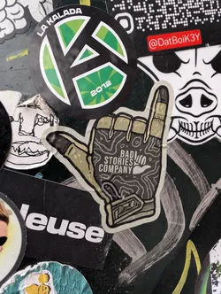 This sticker for 'Bad Stories Company' shows a hand gesture, specifically the 'rock on' or 'devil horns' sign, rendered in a topographic map style with earthy tones. The company's name is printed within the hand's palm area.