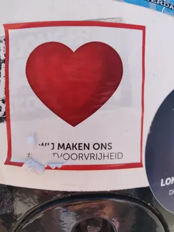 A white square sticker with a red heart in the center and a phrase in Dutch at the bottom. The phrase seems to be incomplete. 