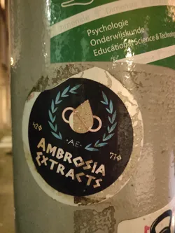 Street sticker Round black and white sticker with the text 'Ambrosia Extracts' in a stylized font. It features a central design of a droplet with interconnected rings, flanked by a laurel wreath. Numbers '428' and '770' are visible on either side of the design. The abbreviation 'AE' is present beneath the central image.