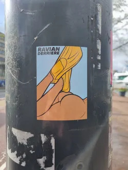 A sticker featuring a stylized illustration of a person's buttocks with a yellow object, possibly a garment, being pulled down. The artist's name, "Ravian Derriere," is printed on the sticker. The style is reminiscent of comic book art or cartoons. 