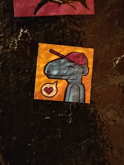 Street sticker A small, blue creature wearing a red baseball cap is featured on this sticker. It has a friendly expression and a small heart-shaped speech bubble beside it, suggesting a message of love or affection. The sticker has a vibrant color scheme with an orange background.