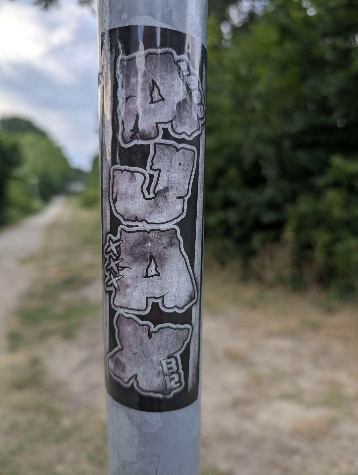 A vertical black sticker featuring stylized grey bubble letters spelling 'AUAX'. Includes small details like 'RAGE' on the top letter, three 'X' marks on the third, and '1312' on the bottom 'X'.
