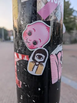 Die-cut sticker depicting a pink, peach-shaped head with a cute face, featuring large anime-style eyes, long eyelashes, rosy cheeks, and a small smiling mouth.
