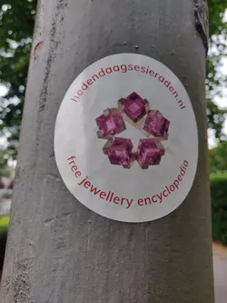 Street sticker Round sticker with a picture of pink gemstones in the center. The text hedentijdagsieraaden.nl is visible at the top.  The text "free jewellery encyclopedia" is visible at the bottom.