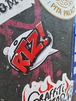 Street sticker A sticker featuring the stylized text "R!Z!" in a red and white comic book style. The text is contained within a speech bubble with a red exclamation point.  The style is reminiscent of pop art and graffiti.
