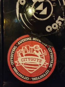 Red and white round sticker with the Cityguys logo.  The logo features a cartoon character holding a hot dog in front of a city skyline. The text "CITYGUYS" is prominently displayed in the center. The words "AWESOME SAUCE" appear above the logo in a smaller font, and "CITYGUYS.NL" is written repeatedly around the edge.
