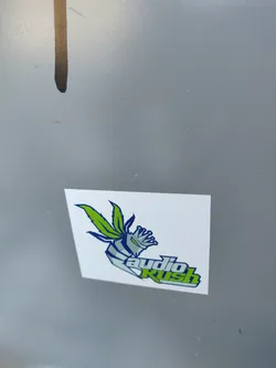 Street sticker A small white sticker with a stylized logo. The logo features a design incorporating elements resembling cannabis leaves and a crowned figure, combined with the text 'audio Rush'.