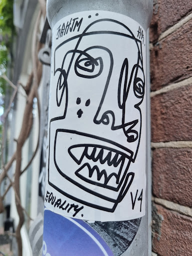 Black and white sticker with a stylized face illustration. The face has sharp teeth and a unique design. The word 'equality' is written at the bottom. The artist's tag is visible at the top and bottom of the sticker.