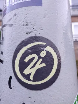 Street sticker A round sticker featuring a dark-colored background with a lighter yellow-cream colored stylized '24' in the center. The '24' has a slightly hand-drawn look.  The number is encircled by a thicker ring of the same lighter color.