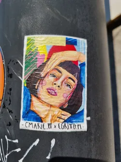 Street sticker A sticker featuring a vibrant, stylized illustration of a woman's face. The art style is bold and graphic, incorporating geometric shapes and bright colors.  The sticker includes the artist's names and likely website addresses: Cmarie.pt and EgriTo.pt.