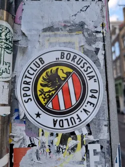 Street sticker A round sticker featuring the logo of Sportclub Borussia Fulda 04 e.V., a German sports club.  The logo depicts a black eagle and red and white vertical stripes on a yellow and black background.