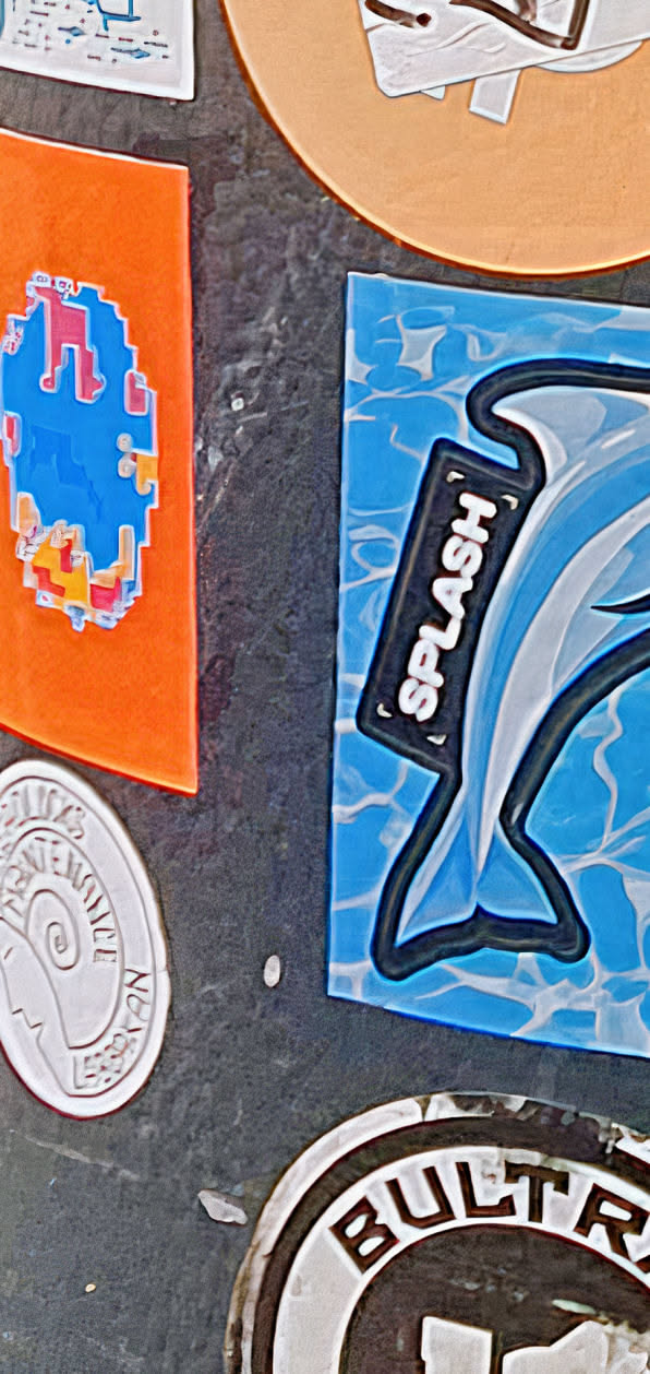 This sticker features a dolphin swimming on a blue, wave-patterned background. The word "SPLASH" is written on a black rectangular shape above the dolphin. The sticker has a bold, outlined design, giving it a cartoonish and eye-catching appearance.