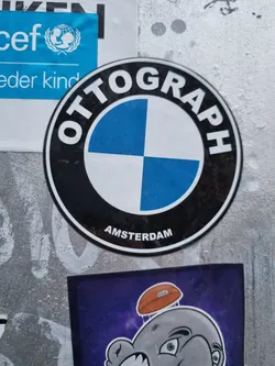 Round sticker with a stylized BMW logo and the word "OTTOGRAPH" around it.  The word "AMSTERDAM" is printed at the bottom of the sticker. 