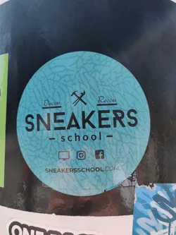 Street sticker Round sticker with a teal cracked-like pattern. It has the text 'Sneakers School' in black uppercase letters with 'Decon' and 'Recon' on either side of crossed hammers. At the bottom, there are icons for a computer monitor, Instagram, and Facebook, followed by the website address 'sneakerssschool.com'.