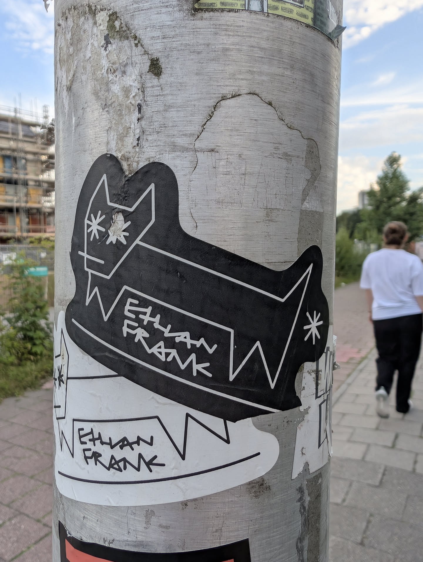 A black die-cut sticker with white line art of a blocky animal character. It features asterisk-shaped eyes and rear detail, with 'ETHAN FRANK' written on its body.