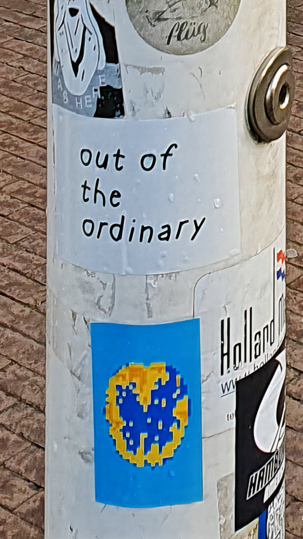 A close-up shot of a pixelated heart sticker on a white pole, surrounded by other stickers. The heart is blue with a yellow outline, set against a bright blue square background. The pole is covered in various stickers.