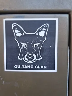 Street sticker A black and white sticker with a stylized image of a dog's head and the text "GU-TANG CLAN" at the bottom. The dog's expression is serious and intense. The sticker has a simple design, suggesting a possible affiliation with a group or brand.