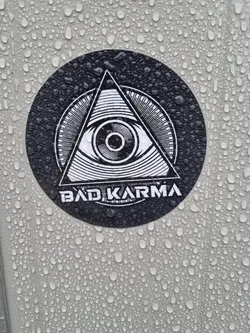 Round black and white sticker with an eye inside a triangle. The text 'Bad Karma' is at the bottom.