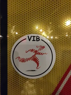 Street sticker A round white sticker with the letters "VIB" at the top and a stylized red running figure at the center. The sticker is affixed to a yellow honeycomb-patterned surface.