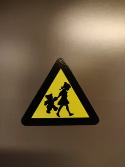 Street sticker This sticker is in the shape of a triangle and depicts a silhouette of a girl walking with her teddy bear.  It has a yellow background and black border, mimicking a warning sign. 