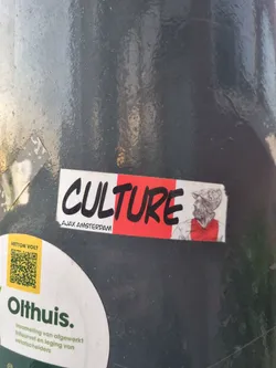 A sticker featuring the word 'CULTURE' in black paint-like lettering on a red background, with a sketch of a man in an Ajax Amsterdam jersey to the right.  The words 'Ajax Amsterdam' are printed below 'CULTURE'.