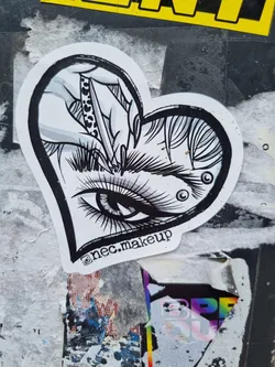 A black and white illustration of an eye with a hand using tweezers to shape its eyebrow, set in a heart-shaped frame. The style is reminiscent of tattoo art. The sticker includes the Instagram handle @nec.makeup in the bottom corner.