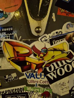 Street sticker A colorful sticker with the words "Rolling Wood" is shown. It's placed on a surface covered with other stickers, creating a layered effect.  The central sticker is predominantly yellow and features a stylized graphic alongside the text.  Other visible text on surrounding stickers includes mentions of 'Value' and 'Ultra Cotton'.