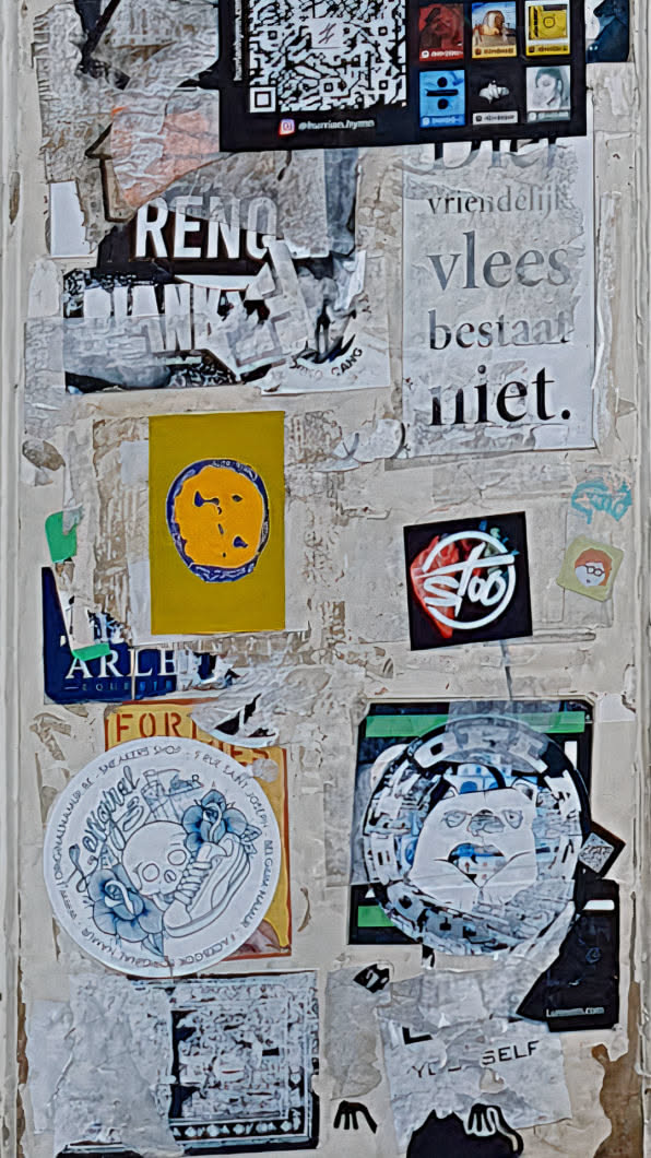 A cluttered wall covered with various stickers and torn posters. The stickers feature diverse designs, including a skull with flowers, abstract patterns, and text in different fonts. The overall aesthetic is chaotic and urban, reflecting the nature of street art.