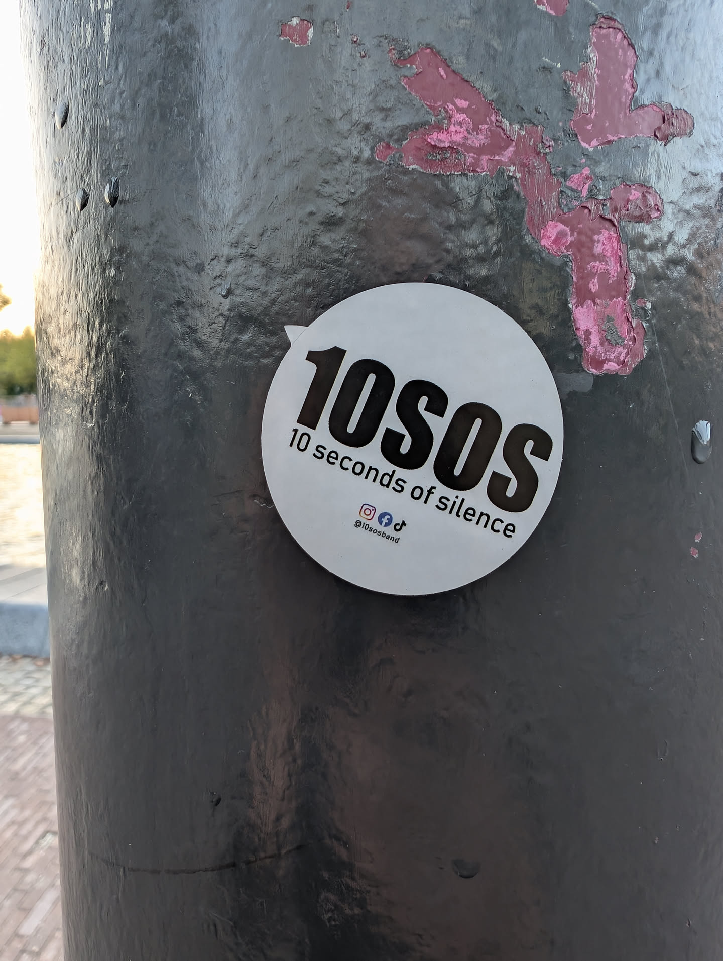 A round white sticker with a small tab on the upper-left. It features bold black text reading '10SOS' and '10 seconds of silence' below it, along with social media icons and the handle '@10sosband'.