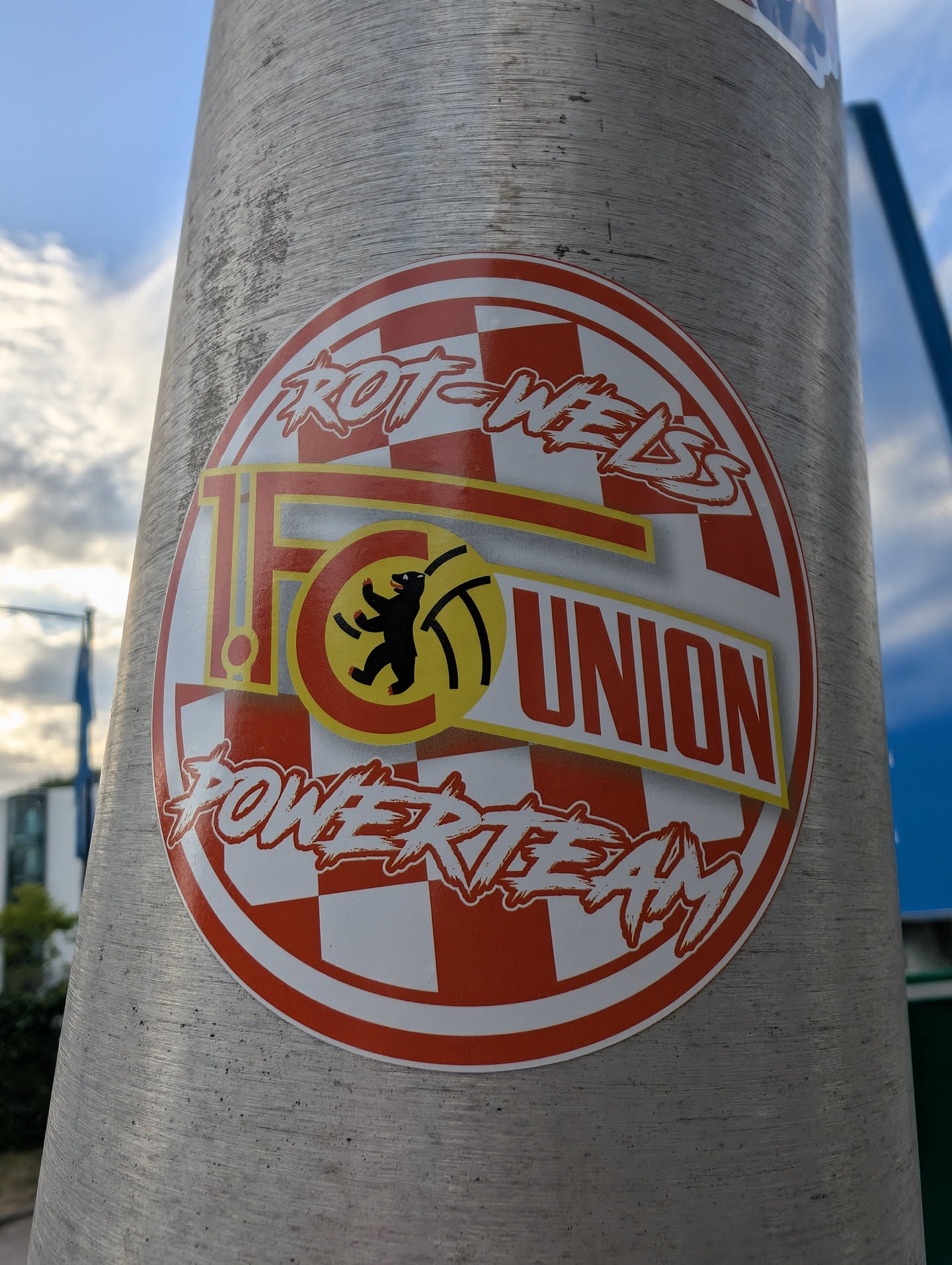 A circular sticker featuring the 1. FC Union Berlin logo over a red and white checkered background. The words 'ROT-WEISS' and 'POWERTEAM' are written in a stylized white font at the top and bottom. The central club logo displays a black bear in a yellow circle alongside the text '1. FC UNION'.