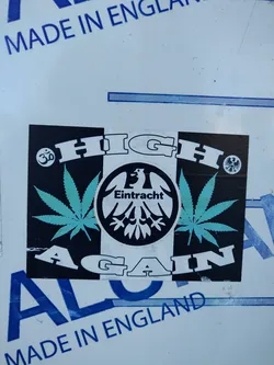 A sticker with a tri-color design featuring cannabis leaves, an eagle emblem with the word 'Eintracht', and the text 'HIGH AGAIN'.  The Om symbol and a German eagle are also present. 