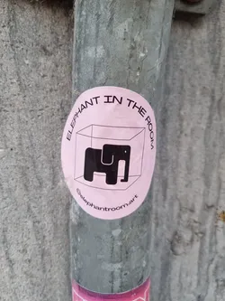 Pink round sticker with a black elephant in a cube. The text "Elephant in the room" is written around the pink circle. The Instagram handle @elephantroom.art is visible at the bottom.