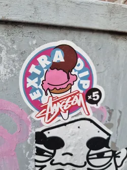 A round sticker featuring an ice cream cone with extra chocolate dip. The sticker also has the text "EXTRA DIP" and a logo that looks like a stylized signature.  The number "x5" is visible on the sticker.