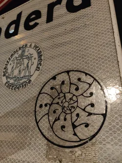 Street sticker A beautifully detailed sticker of a nautilus shell. The design is simple yet elegant, with a black outline against a clear background.  It seems to have a slightly glittery finish. The sticker is affixed to what looks like a reflective surface.