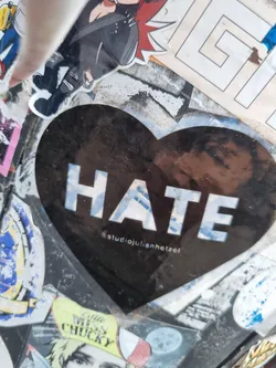 Street sticker A black heart-shaped sticker with the word HATE written in white capital letters.  The Instagram handle @studiojulienhetzel is visible at the bottom of the sticker. The sticker appears to be placed on a surface with other stickers.