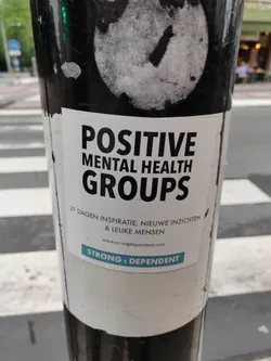 A sticker promoting positive mental health groups.  The sticker features the text "POSITIVE MENTAL HEALTH GROUPS", followed by a tagline in Dutch: "21 DAGEN INSPIRATIE, NIEUWE INZICHTEN & LEUKE MENSEN" (21 days of inspiration, new insights & nice people). A website address, www.strongdependent.com, is included along with the text "STRONG & DEPENDENT".