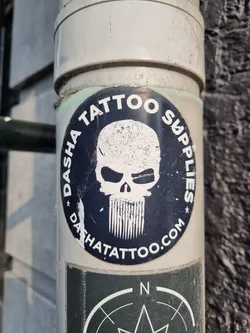 A round sticker with the text "DASHA TATTOO SUPPLIES" encircling a skull graphic with a beard. The website dashatattoo.com is also visible. The sticker is affixed to a pipe.