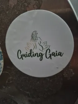 Street sticker White round sticker with a logo of a woman sitting with leaves around her and the text Guiding Gaia written in a green cursive font.