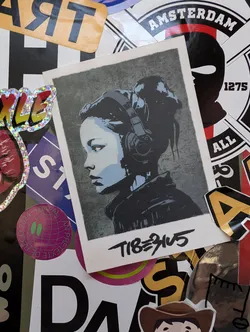 Street sticker A sticker featuring a stylized portrait of a girl wearing headphones. The art style is reminiscent of street art or stencil work, with a slightly gritty texture. The sticker has the artist's tag 'TIB3945' written underneath the artwork.
