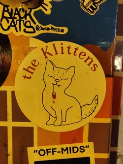Street sticker Yellow round sticker with an illustration of a cat and the text "the Klittens" on top.  At the bottom, there's a smaller black rectangular sticker that says "Off-Mids".