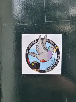 Street sticker A sticker with an illustration of a pigeon carrying a piece of paper in its beak. The sticker has a circular design with the text "No Justice No Peace" written on the upper part of the circle and "Fuck The Police" on the lower part.  In the center is a cartoon pigeon flying.  The artist's signature, "wandelcluboso", is also included on the sticker.