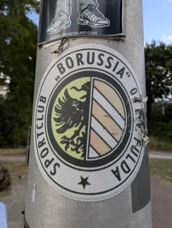 Street sticker A round sticker displaying the SC Borussia Fulda logo. It features a split inner shield with a black eagle on the left and diagonal stripes on the right, surrounded by the club's name in black text.